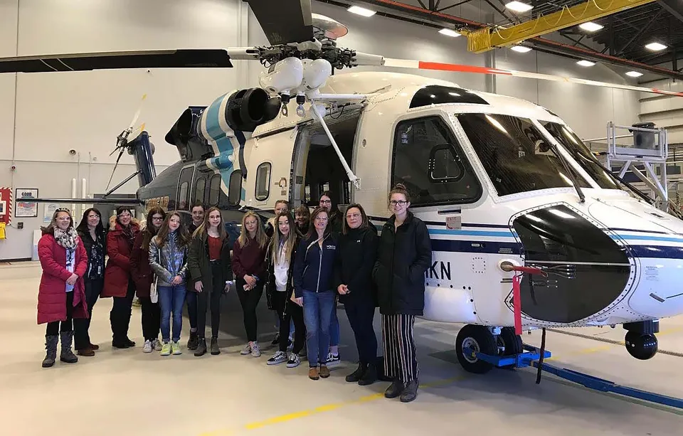 Un gruppo di studenti della Mount Pearl Senior High School sta davanti a un grande elicottero bianco in un padiglione espositivo.