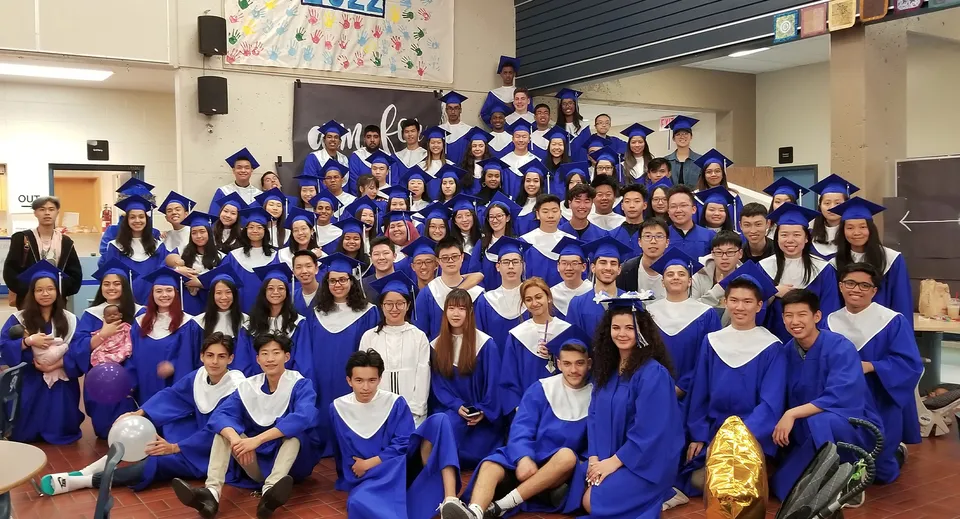 Un grande gruppo di diplomati della R.C. Palmer Secondary School posa con toghe blu all'interno di un'aula.