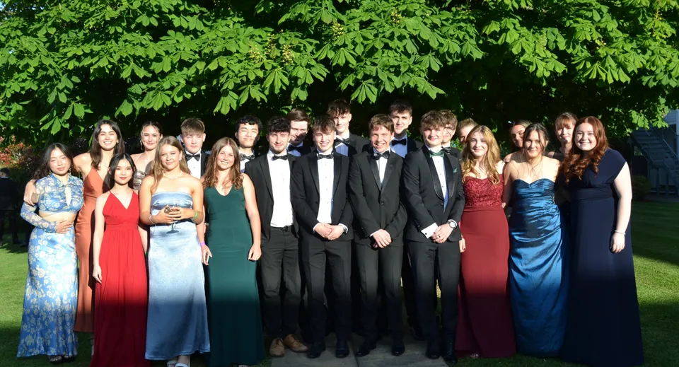 Un gruppo di persone in abiti formali si trova davanti al fogliame verde nell'area della West Buckland School.