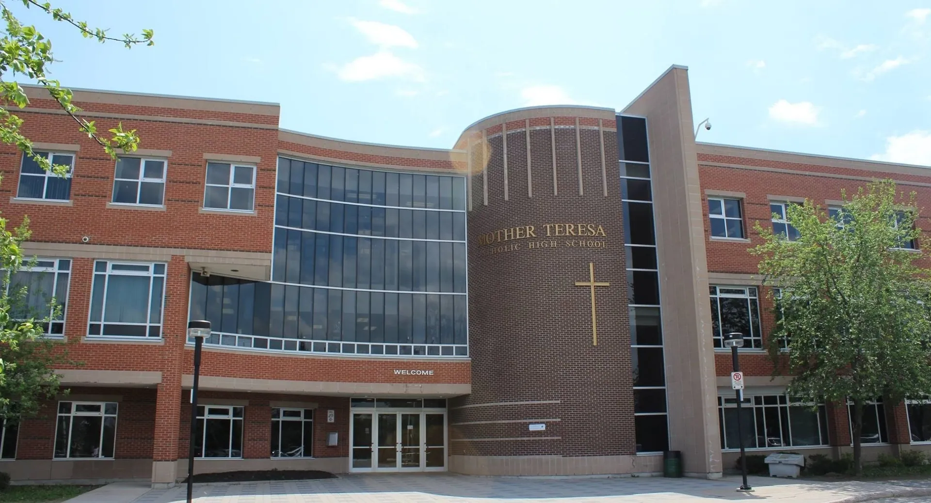 L'edificio a più piani della St. Mother Teresa High School con una facciata a vetrata curva è circondato da alberi.