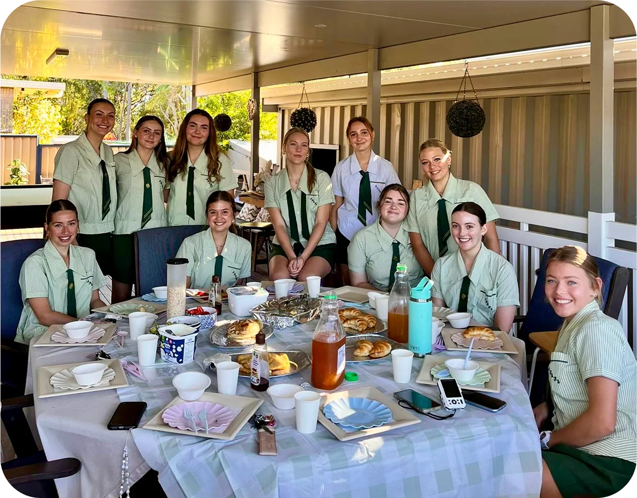 Grupo de alumnas con uniforme escolar desayunando juntas alrededor de una mesa en una terraza cubierta