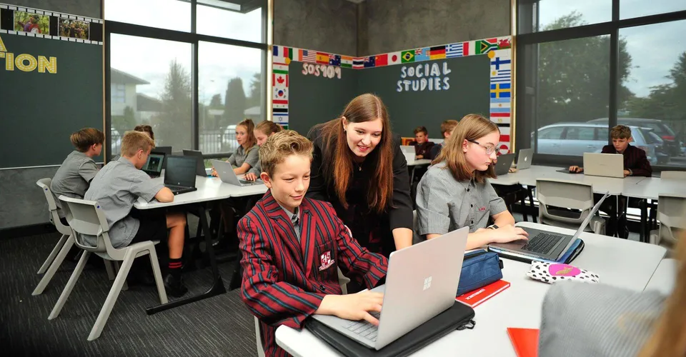 Studenti della Lincoln High School lavorano in aula con laptop e bandiere internazionali durante la lezione di studi sociali.