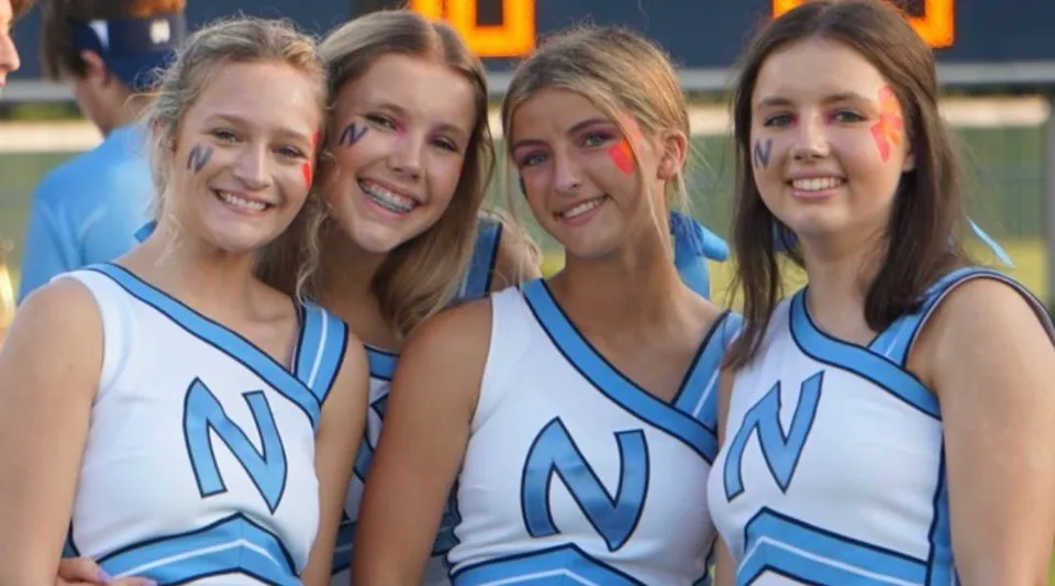 Quattro studentesse in divisa da cheerleader con la lettera N posano insieme davanti a un edificio del campus della Northpoint Christian School.