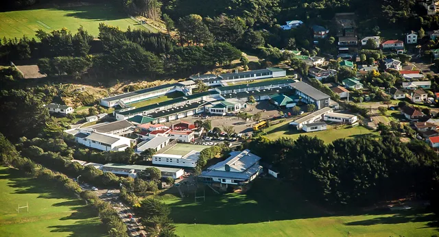 Vista aerea del campus dell'Onslow College con diversi edifici, piscine e tanto verde circondato da colline boscose.