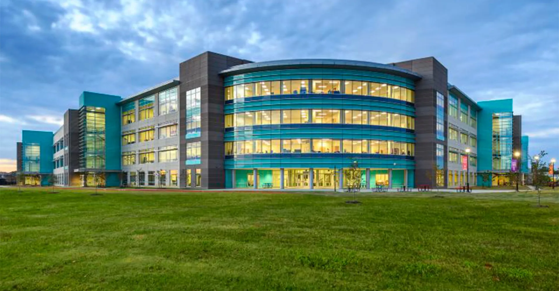 L'edificio moderno a più piani della British International School Houston con una facciata curva in vetro sorge su un prato verde sotto un cielo nuvoloso.