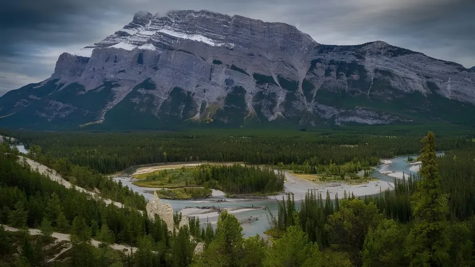Un fiume scorre attraverso una foresta di conifere davanti a una montagna nella regione della Crescent Heights High School.