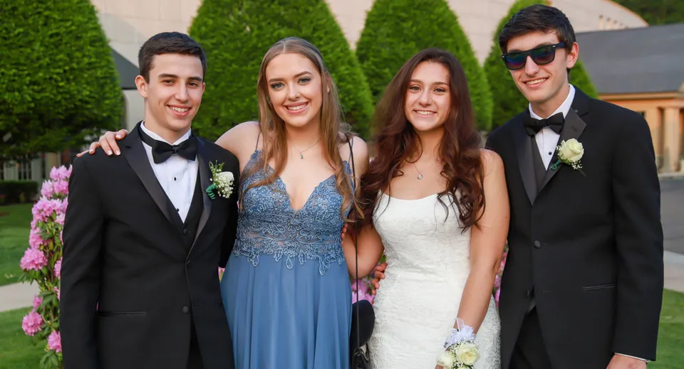 Quattro giovani della Bandon Grammar School si mettono in posa insieme in un giardino con piante verdi e fiori.