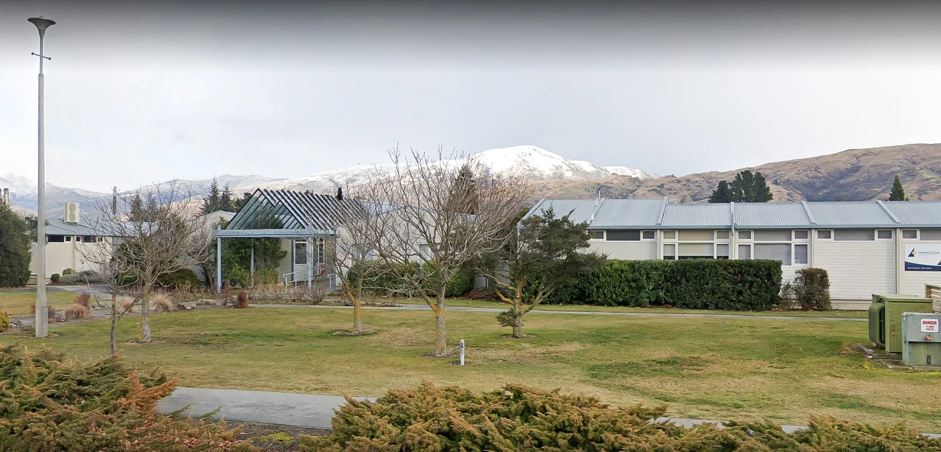 Un parco con padiglione e alberi nel campus del Cromwell College davanti a montagne innevate sullo sfondo.