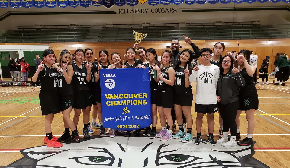 Le studentesse della Killarney Secondary School festeggiano la vittoria del campionato di basket con coppa e striscione in palestra.