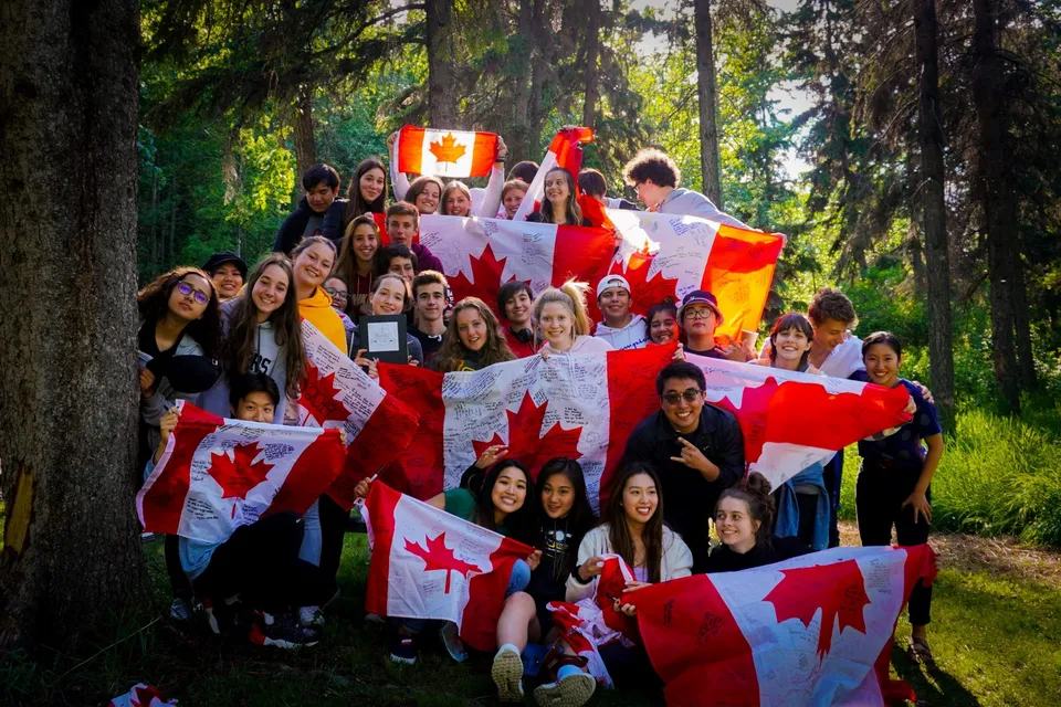 Studenti delle Red Deer Public Schools festeggiano nel bosco con bandiere canadesi durante un evento patriottico.
