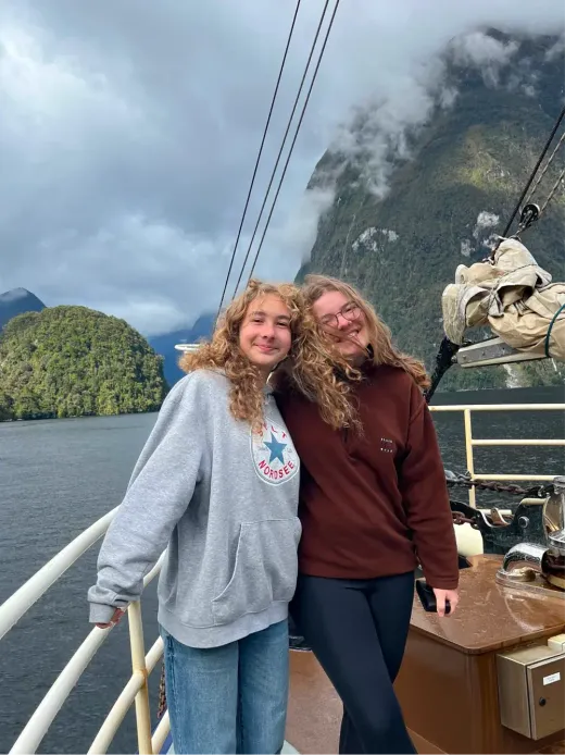 Zwei lächelnde Mädchen auf einem Boot in einem Fjord Neuseelands zwischen wolkenverhangenen Bergen