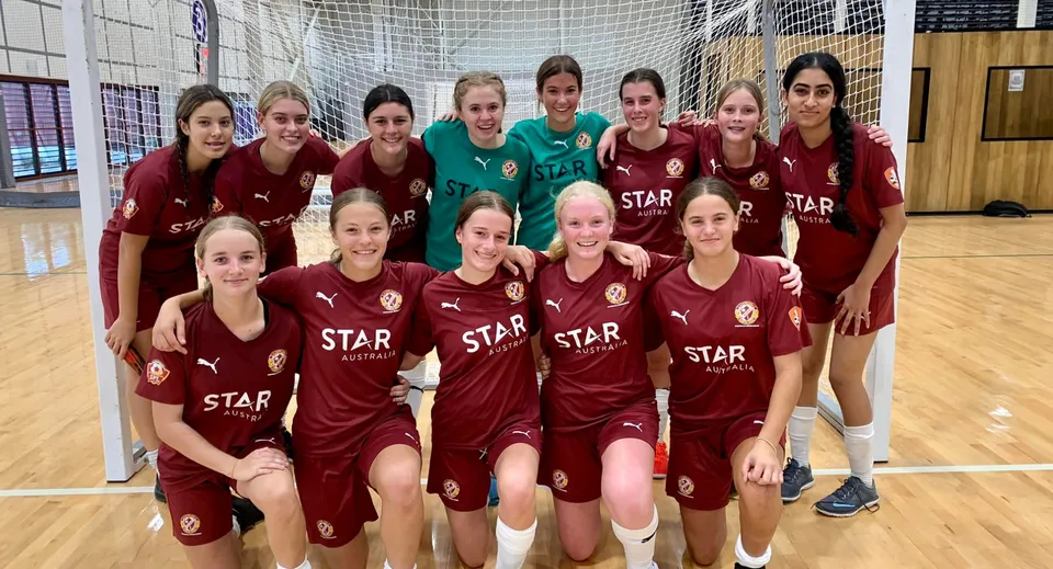 La squadra di calcio della Cleveland District State High School posa insieme nella palestra in maglie rosse e bianche con il logo STAR.