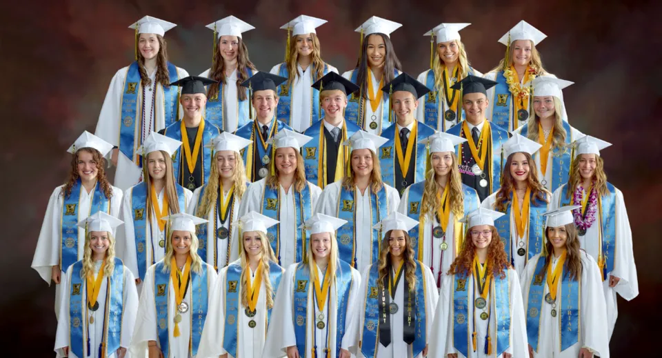 Un gruppo di diplomati della Wasatch Academy in toghe blu e gialle su sfondo rosso.