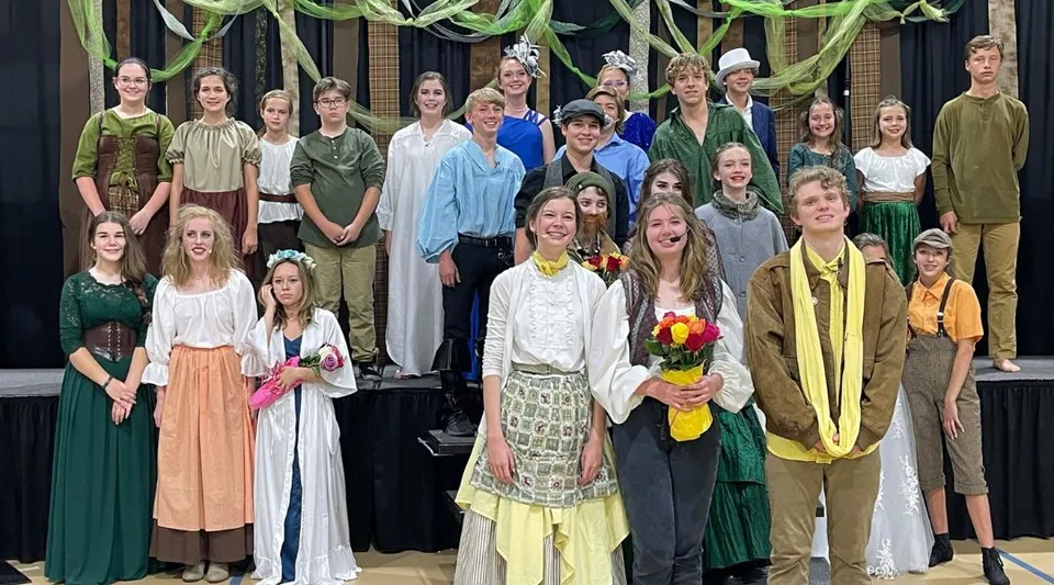 Un gruppo di giovani studentesse della Bayshore Christian School si trova su un palco davanti a uno sfondo scuro con decorazioni.