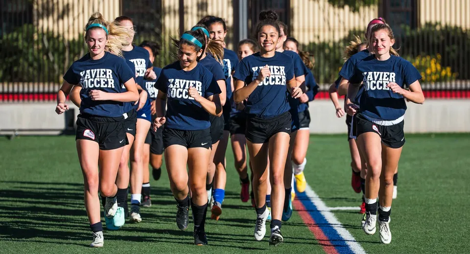 Un gruppo di giovani giocatrici della Xavier College Preparatory High School corre insieme sul campo da calcio.
