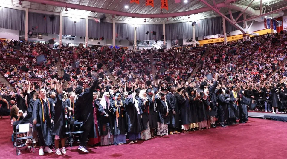 Gli studenti delle Eden Prairie Schools si radunano con le toghe da diploma durante una cerimonia in un grande salone.