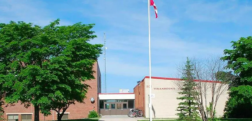 La bandiera sul pennone sventola davanti all'edificio in mattoni della Transcona Collegiate, circondato da alberi verdi.