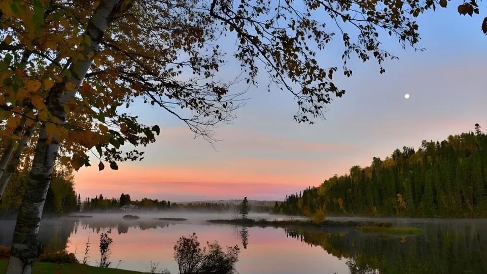 Un lago con alberi dai colori autunnali e una mezza luna in cielo vicino al College Saint-Bernard.
