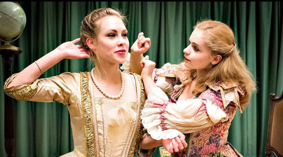 Due donne in costumi d'epoca portano in scena uno spettacolo teatrale davanti a un sipario verde nel campus della The Yehudi Menuhin School.