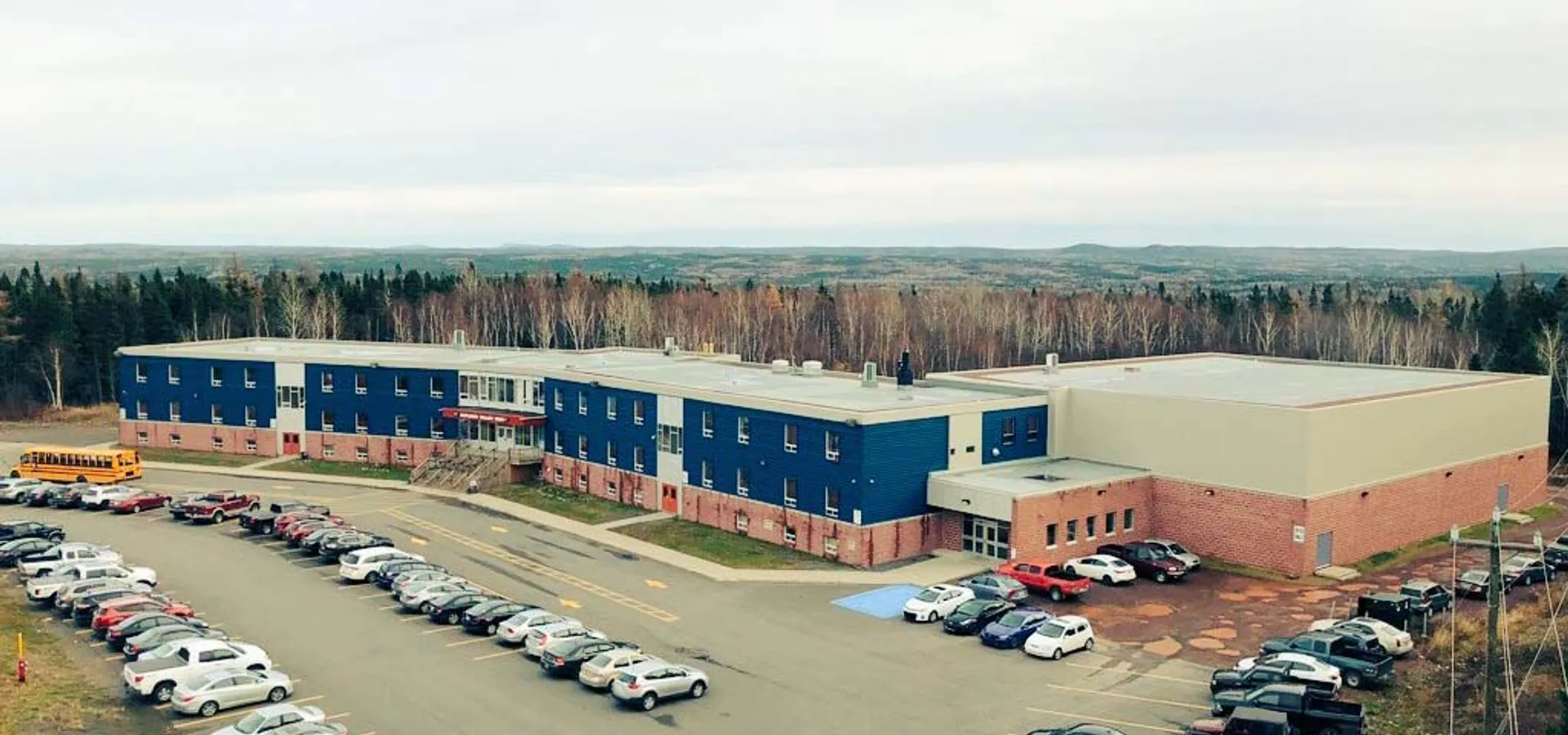 Il grande complesso edilizio della Exploits Valley High School con un parcheggio in primo piano e il bosco sullo sfondo.