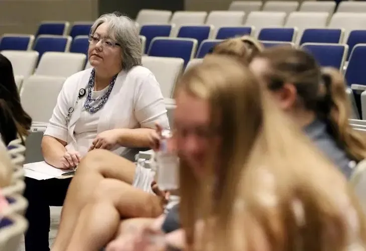 Dos mujeres están sentadas en la sala de conferencias de la Pleasant Valley Secondary School ante filas de asientos azules.