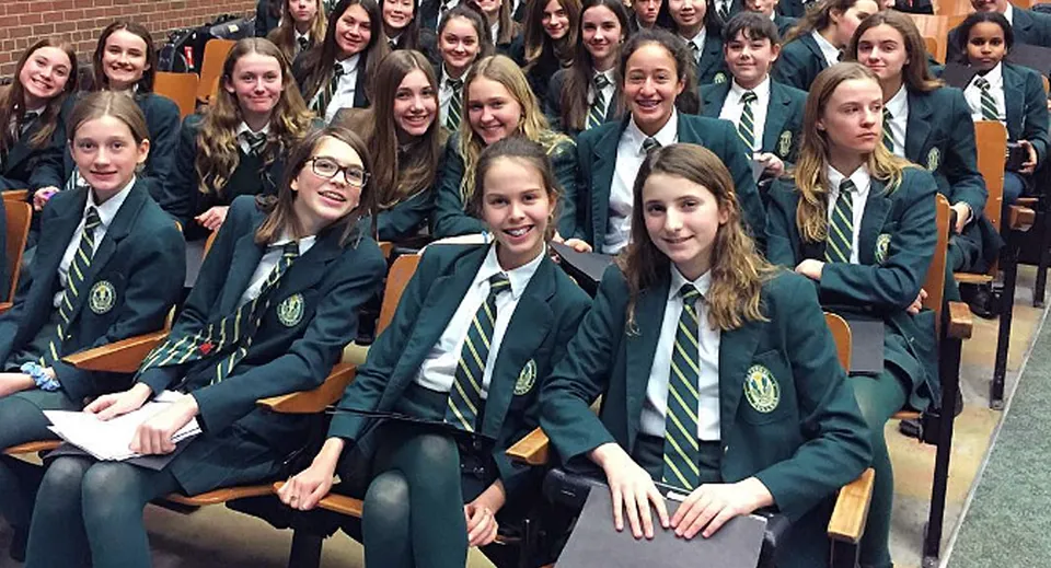Un gruppo di studenti e studentesse in divisa scolastica siede in fila e sorride alla fotocamera nel campus del Sir John A. Macdonald Collegiate Institute.