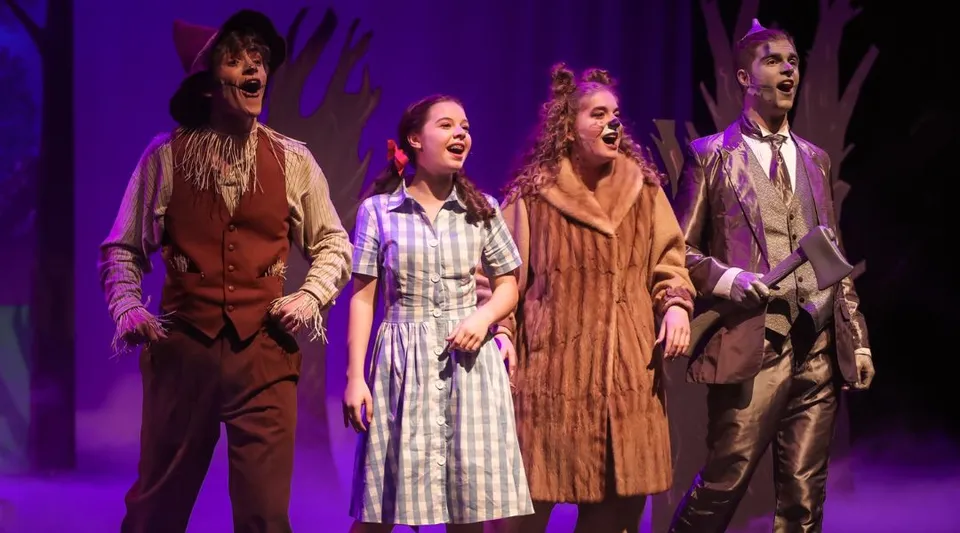 Un gruppo di quattro persone in costume si esibisce sul palco della Cincinnati Christian Schools davanti a uno sfondo viola.