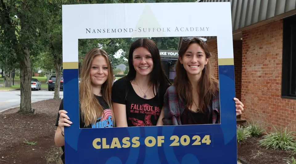 Tre studentesse posano davanti a un cartello della Nansemond-Suffolk Academy con la scritta Classe 2024.