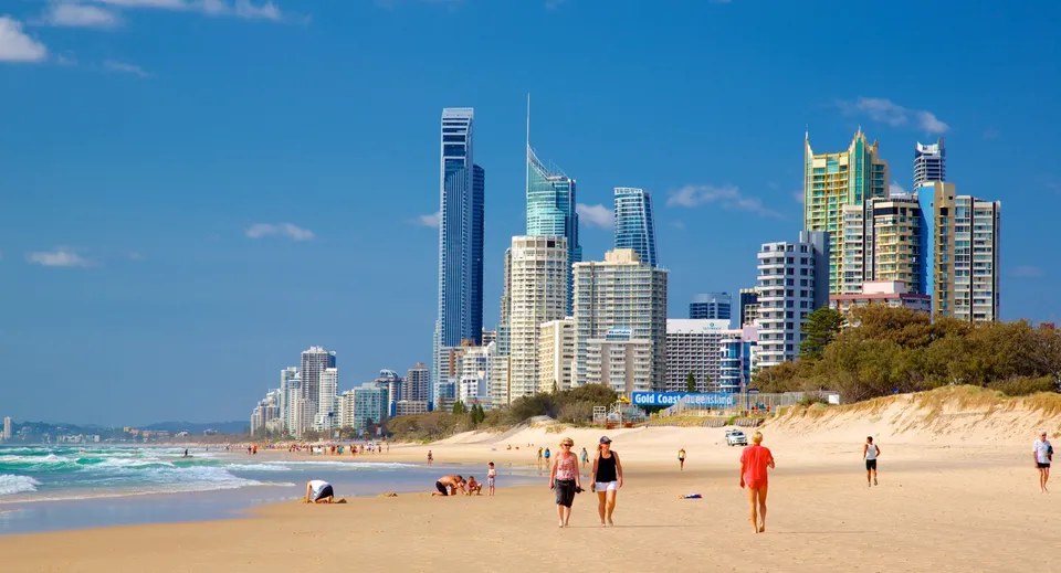 Persone passeggiano su una spiaggia soleggiata con un moderno skyline sullo sfondo vicino alla Keebra Park State High School.