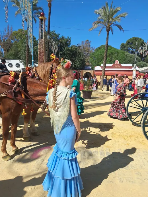 Ragazza in abito da flamenca azzurro alla feria spagnola, accanto a una carrozza trainata da cavalli