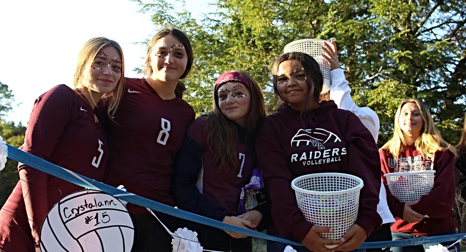 Un gruppo di studentesse della Washington Academy si trova nel bosco con una rete da pallavolo in mano.