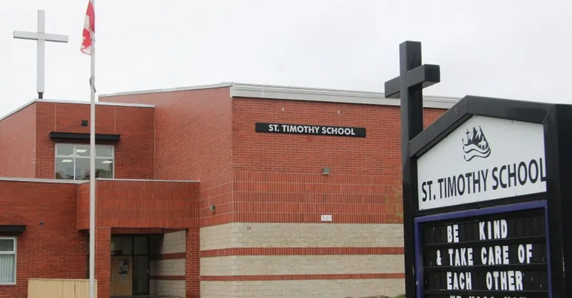 L'edificio principale in mattoni rossi della St. Timothy High School mostra chiaramente il nome della scuola accanto a una bandiera e a una grande struttura a forma di croce.