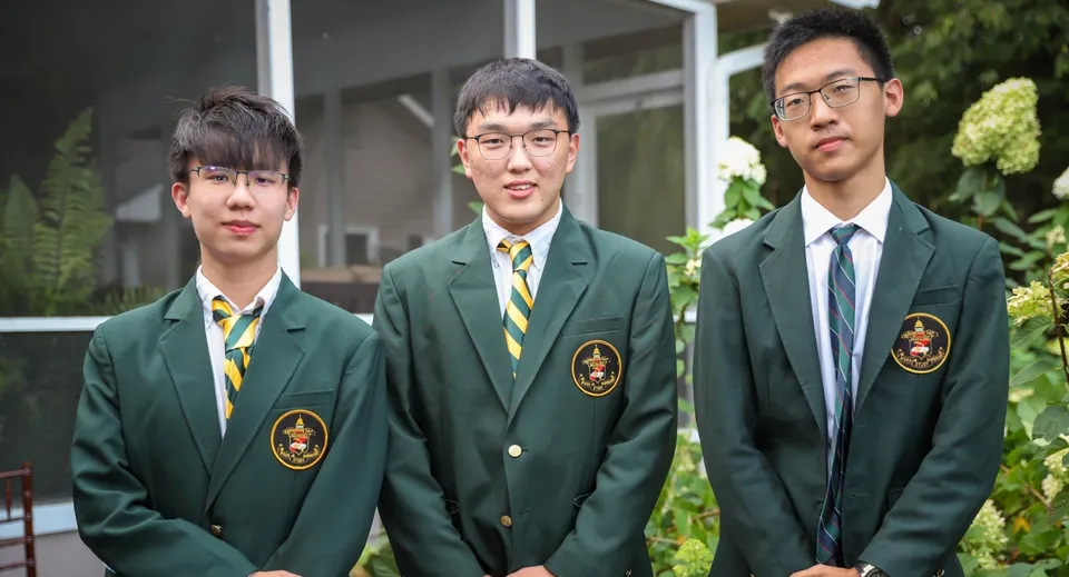 Tre studenti della Rabun Gap-Nacoochee School sono in piedi davanti a un edificio con un giardino sullo sfondo.