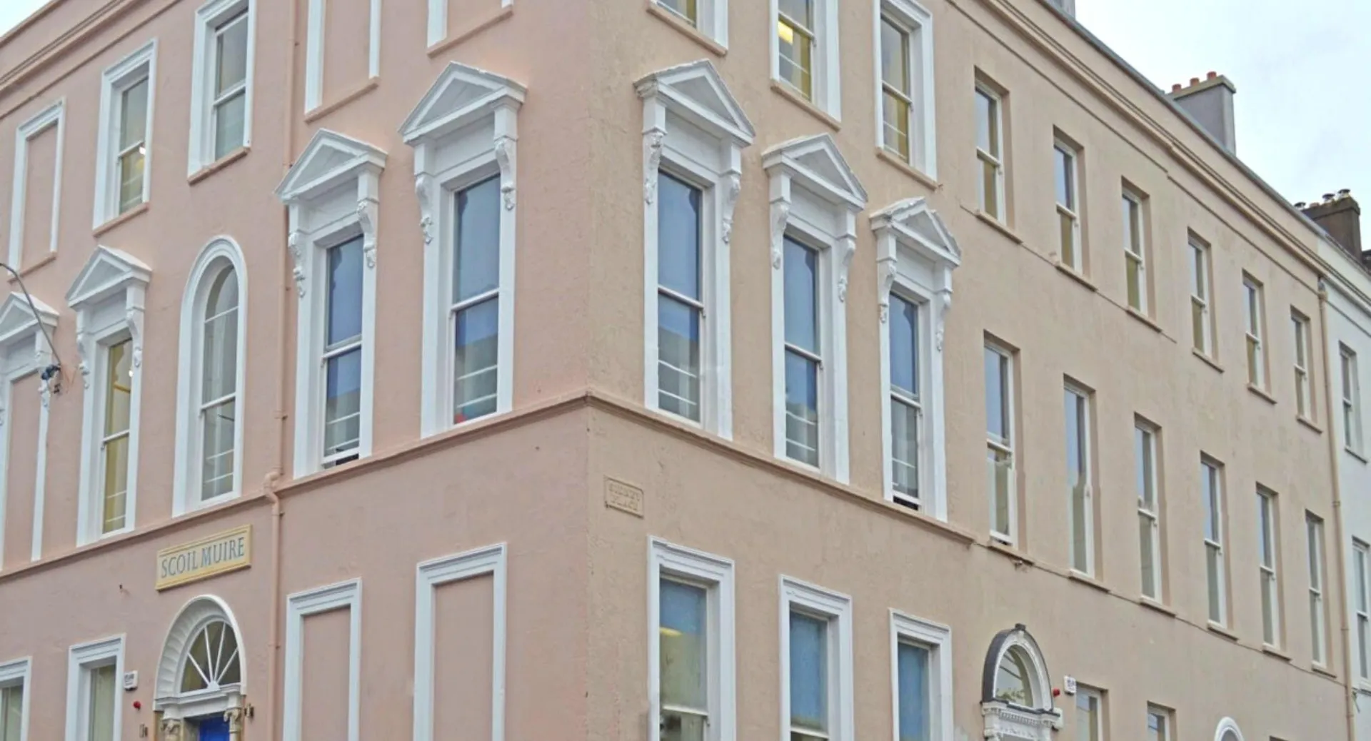 L'edificio a più piani della Scoil Mhuire Cork con grandi finestre e facciata rosa in un contesto urbano.