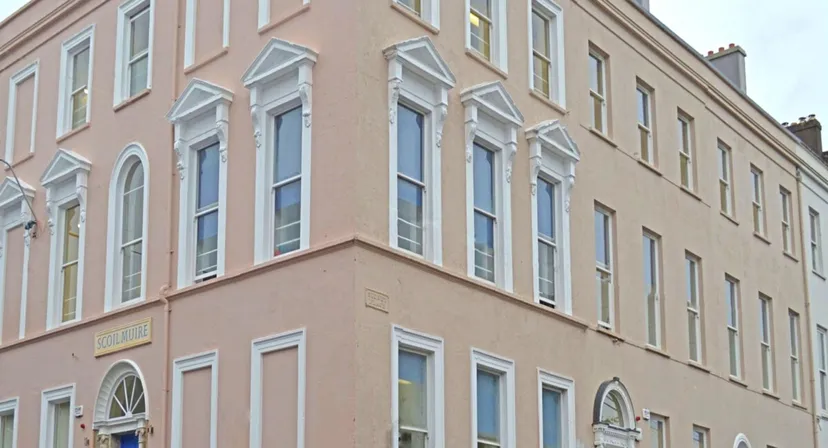 L'edificio a più piani della Scoil Mhuire Cork con grandi finestre e facciata rosa in un contesto urbano.