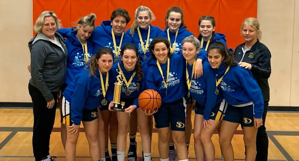 Un gruppo di giocatrici di basket della Spectrum Community Secondary School tiene una coppa e un pallone da basket nella palestra.