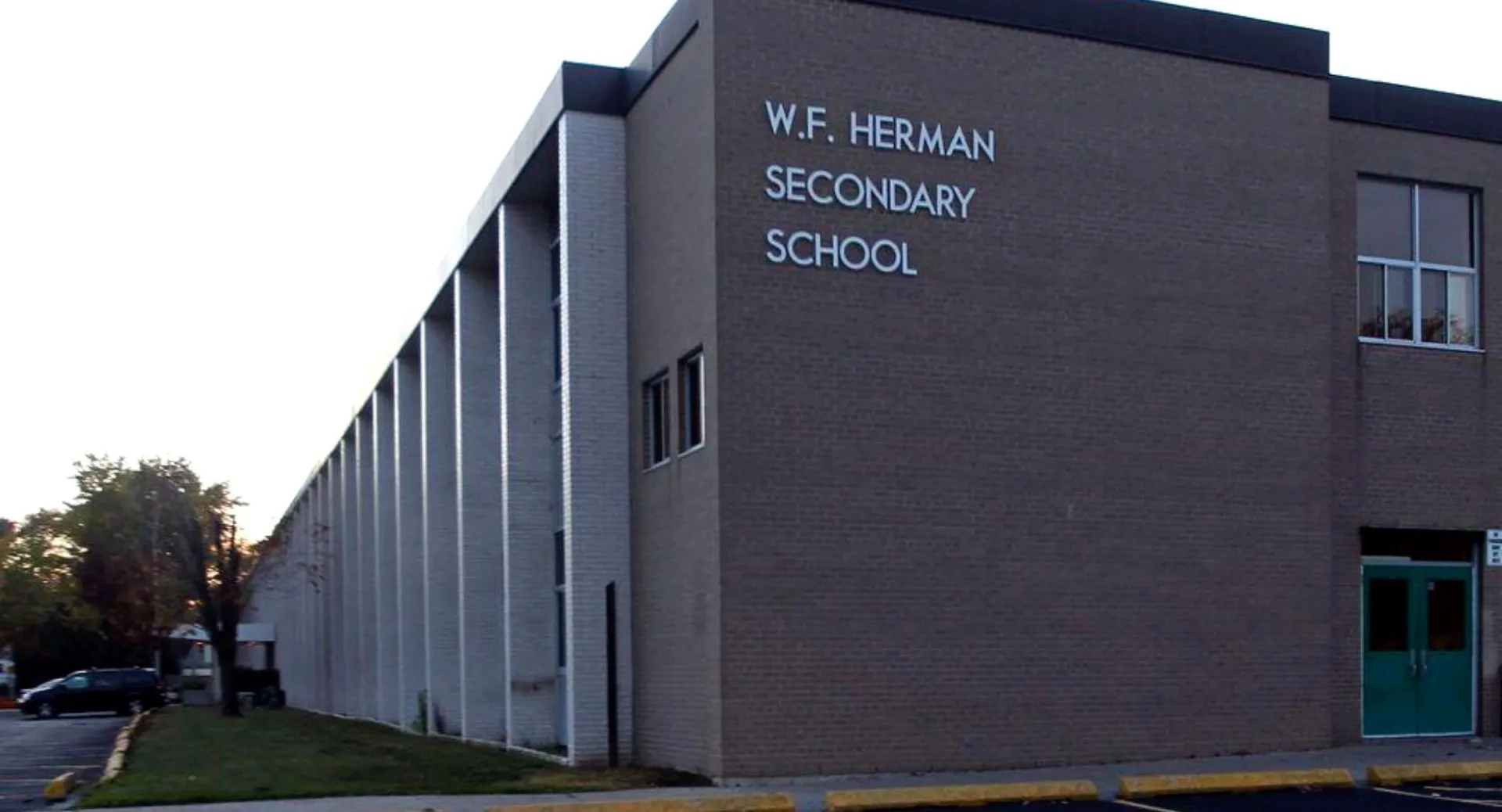 L'edificio della W.F. Herman Academy Secondary School con l'insegna della scuola sulla facciata e un parcheggio in primo piano.