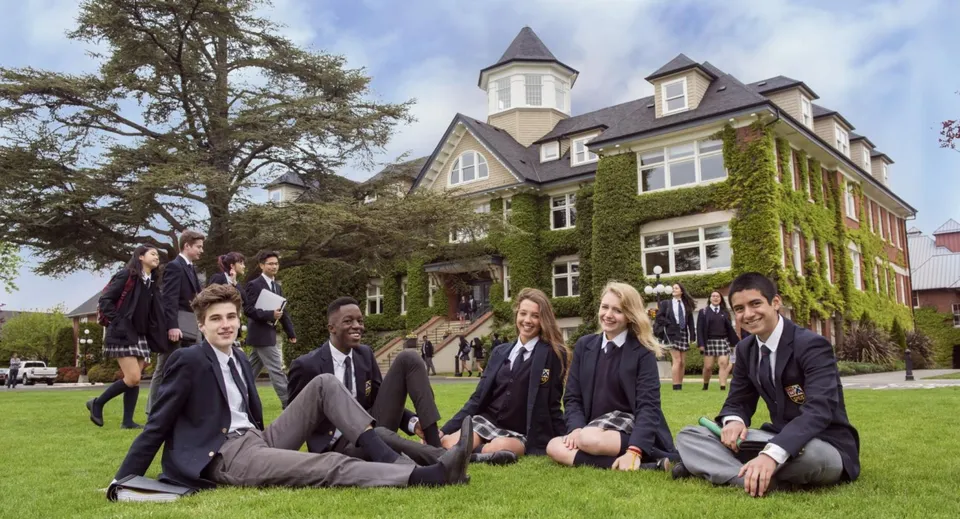 Studenti della St. Michaels University School siedono in divisa scolastica sul prato davanti all'edificio principale ricoperto d'edera.