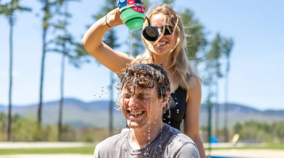 Una donna spruzza per gioco dell'acqua sul viso di un uomo all'aperto nel campus della Gould Academy.