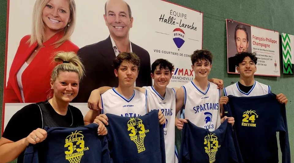 Un gruppo di giovani giocatori di basket posa davanti a uno striscione con candidati politici nel campus della Chateauguay Valley Regional High School.