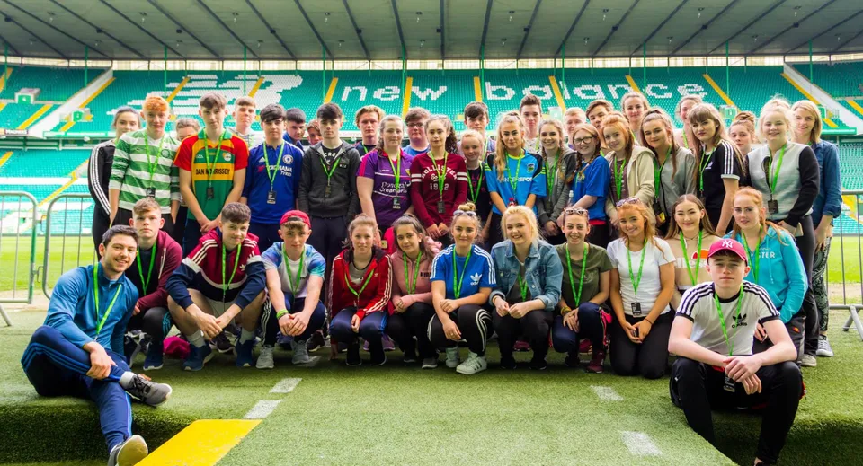 Un gruppo di studenti e studentesse si trova sul campo sportivo del Coláiste an Chreagáin con maglie sportive e abiti casual.