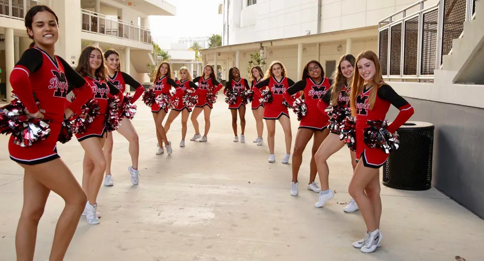 Un gruppo di cheerleader con uniformi rosse e nere e pompon si trova nel campus della Miami-Dade County Public School.