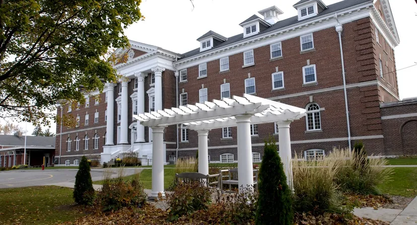 L'edificio in mattoni con facciata a colonne bianche del Pickering College si trova circondato da alberi e cespugli.