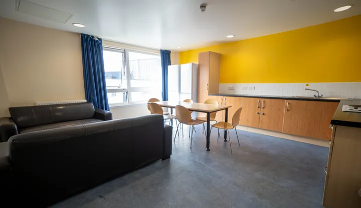 Cocina y salón compartidos de la residencia con pared amarilla, sofá y mesa de comedor