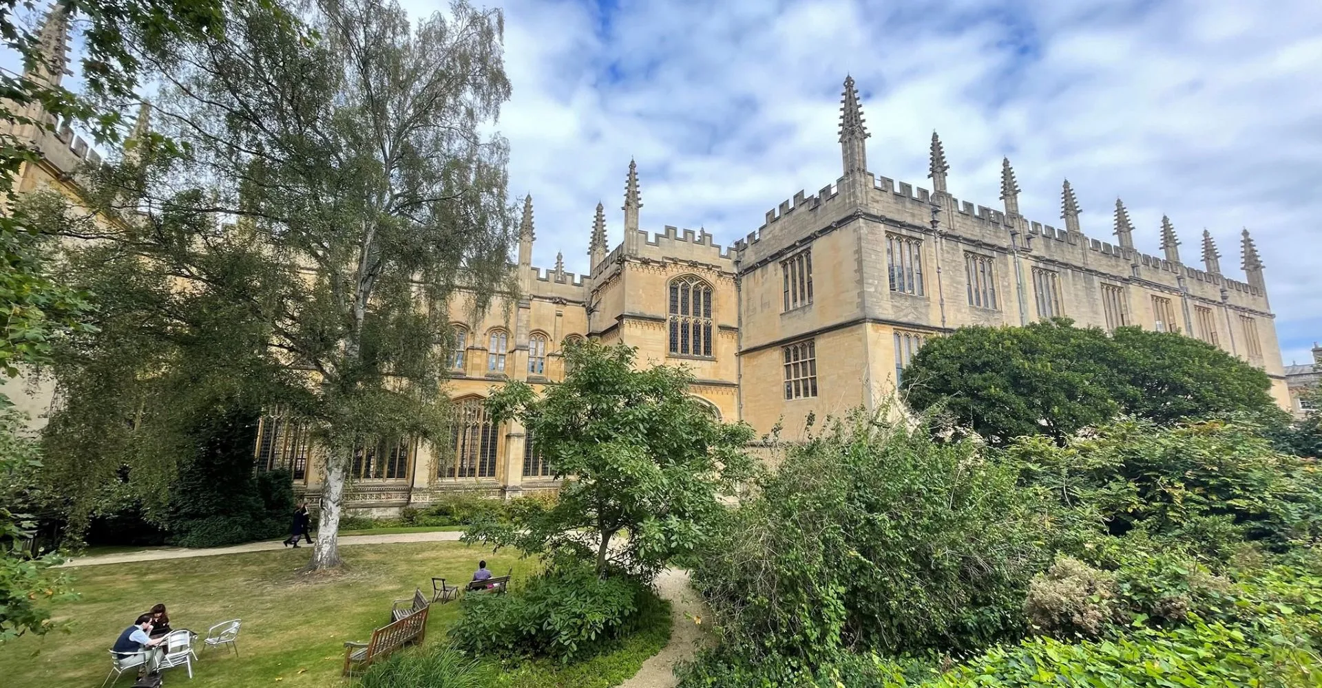 Davanti alla cattedrale gotica nel campus dell'Exeter College, una persona è seduta su una panchina tra gli alberi.