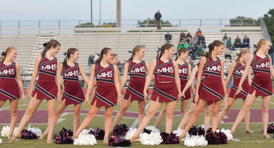 Un gruppo di cheerleader in uniformi coordinate si trova sul campo sportivo del Milford Public School District davanti agli spettatori.