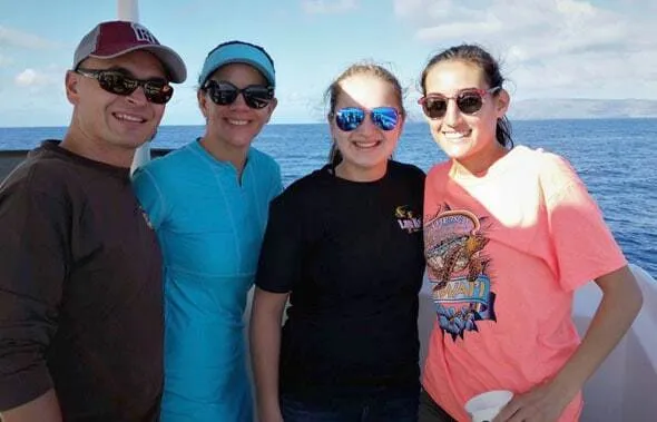 Cuatro personas con gafas de sol sonríen en la cubierta de un barco en alta mar