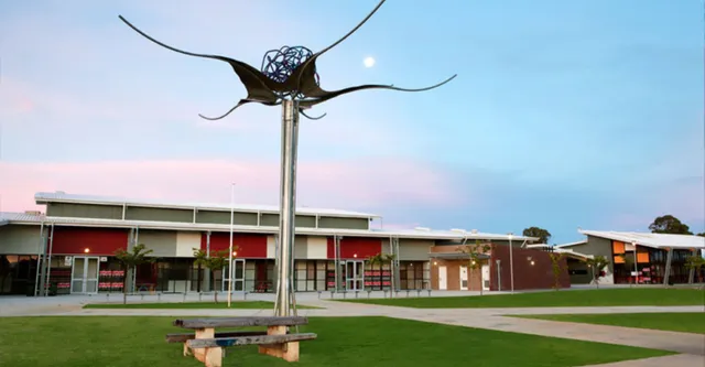 Una grande scultura in metallo a forma di farfalla si erge su un alto palo davanti al moderno complesso del Gilmore College.