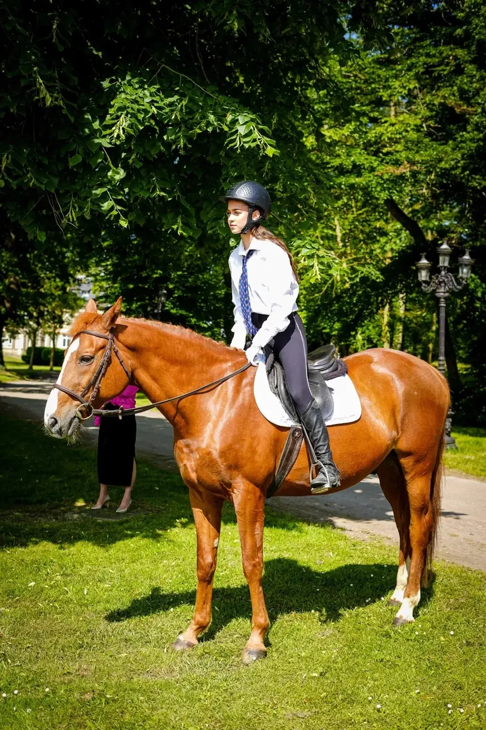 Una persona in cappotto bianco cavalca un cavallo baio in un parco all'interno del campus della Ecole des roches.