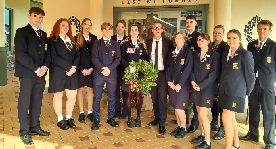 Un gruppo di studenti della Thames High School si trova insieme in un corridoio davanti a un cartello con la scritta 'Lest We Forget'.